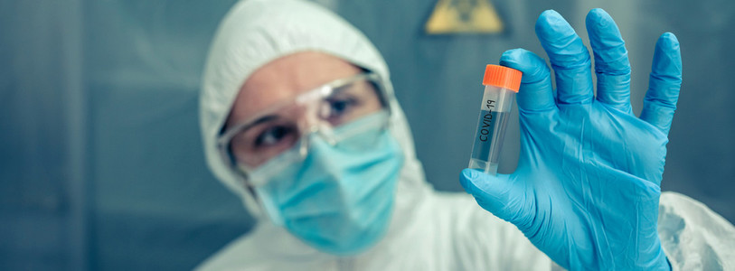 Scientist with protection suit looking vial in the laboratory