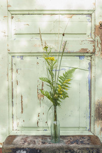 Yellow and green flower stems in vase by door with chipped paint