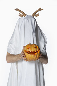Portrait playful man in sheet costume holding jack o lantern