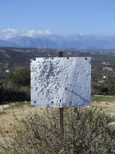 Bullet holes in blank white sign on sunny hilltop