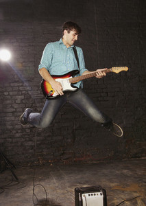 Teenage boy playing electric guitar and jumping above amplifier