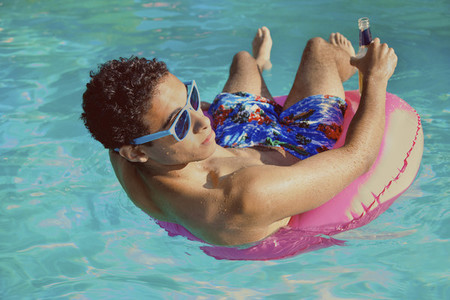Teenage boy relaxing in inflatable ring in sunny summer swimming pool
