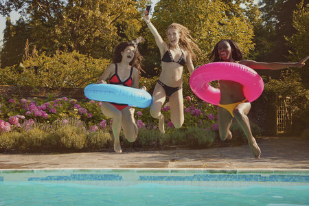 Playful teenage girl friends jumping into sunny summer swimming pool