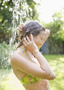 Young woman in bikini top standing under outdoor shower on summer patio