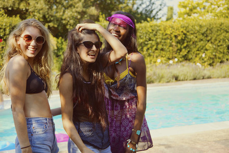 Portrait happy teenage girl friends at sunny summer poolside