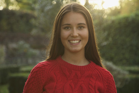Portrait happy teenage girl in red sweater in park