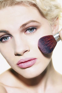 Portrait glamourous young woman applying blush with brush
