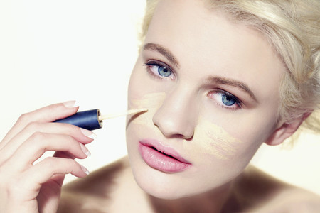 Portrait young woman applying concealer makeup to face