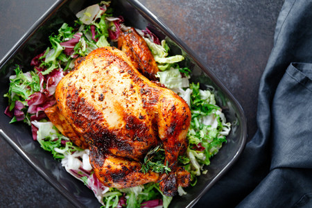 Top view of whole roasted chicken with fresh salad in black dish