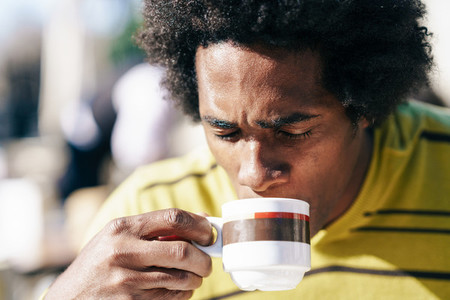 Black man enjoying coffee in cafe while sitting at the table outdoors