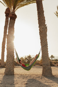 Young woman lying in his hammock among palm trees on the beach