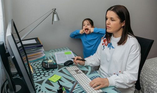 Woman telecommuting making a video conference with her daughter grimacing behind