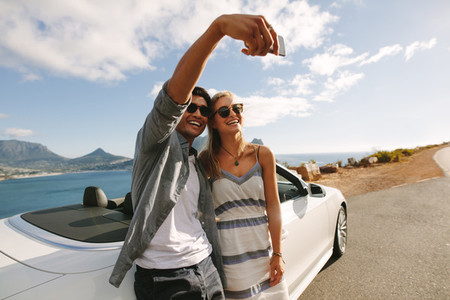 Couple standing by their car taking selfies