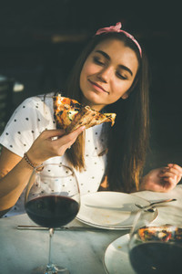 Happy caucasian woman eating pizza and drinking wine