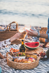 Couple having picnic at seaside and clinking glasses with wine
