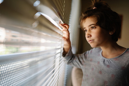 Nine years old girl looking out the window through the blinds