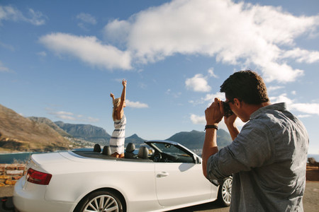 Man photographing woman in convertible car
