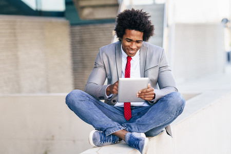Black Businessman using a digital tablet sitting near an office building