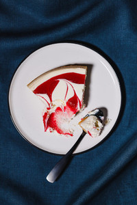 Creative minimalist food photography  strawberry cheesecake on a white plate with spoon over dark blue background