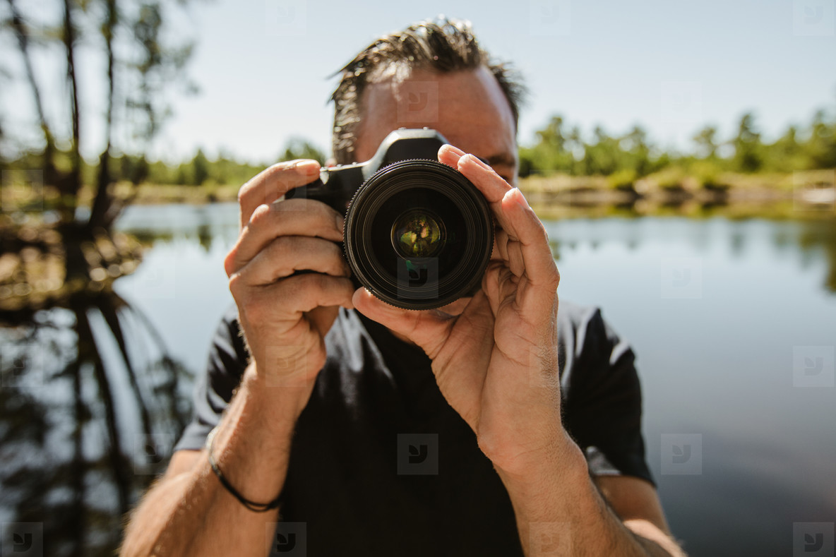 Male photographer by the lake taking pictures with a camera