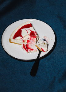 Creative minimalist food photography  strawberry cheesecake on a white plate with spoon over dark blue background