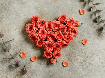 Heart is made from fresh mini coral roses on a beige textured background