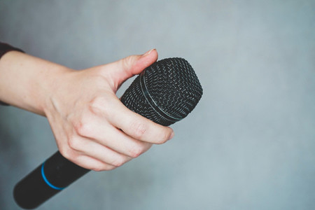 Hand holding a microphone against gray background