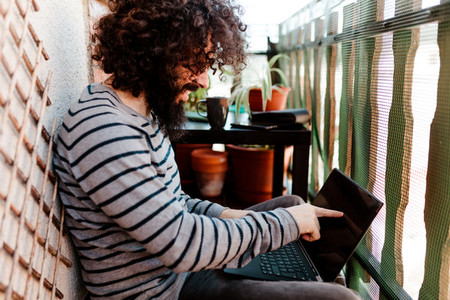 Young afro caucasian with laptop in his balcony
