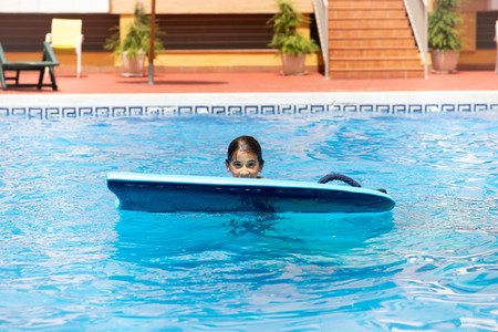 Cute girl playing with a bodyboard in a swimming pool