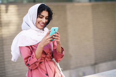 Young Arab woman wearing hijab texting message with her smartphone