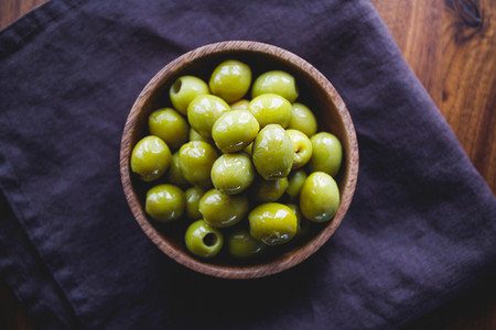Green olives in a wooden bowl on a table  top view