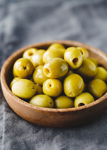 Green olives in a wooden bowl on a table  macro photography
