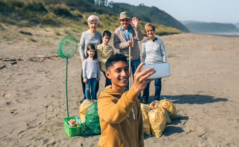 Young man taking selfie to group of volunteers after cleaning beach