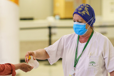Woman pouring disinfectant gel on people entering the hospital