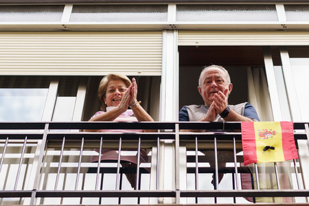 Older couple clapping in the window in support of people against the coronavirus