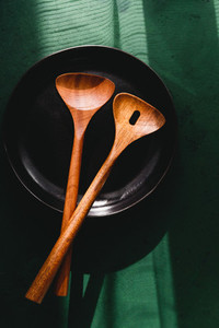Wooden kitchen tools in a black plate over green background