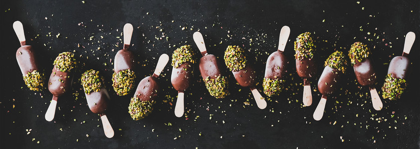 Chocolate glazed ice cream pops over black background  wide composition