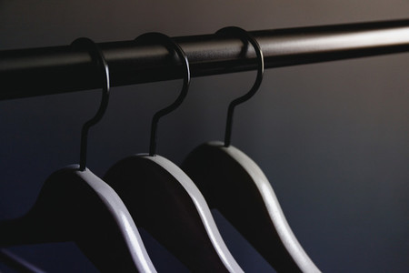Grey hangers without clothes on a crossbar against black wall