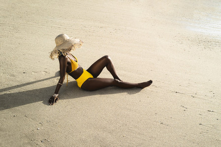 Woman in bikini with sun hat sitting on the beach
