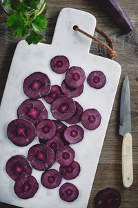 Overhead view on slices of raw purple carrot on a white marble board over kitchen table