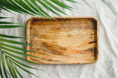 Wooden tray is made from mango tree on a linen cloth decorated palm leaf  Eco friendly and summer mock up