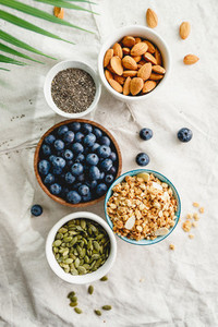 Top view of breakfast ingredients like cereal  almond  blueberry  pepitas and chia seeds on a linen cloth decorated with palm leaf