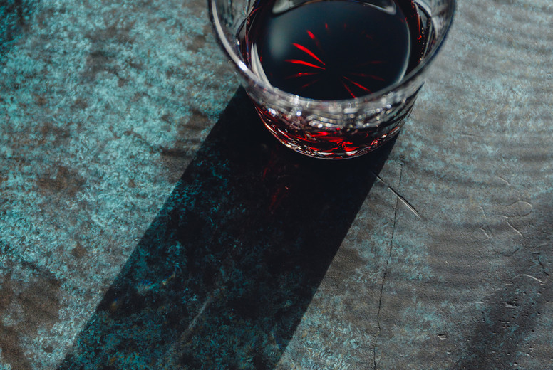 Creative image of red cocktail on a dark blue background under sunlight with contrast shadows.