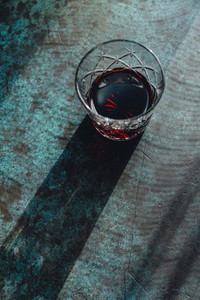 Creative image of red cocktail on a dark blue background under sunlight with contrast shadows