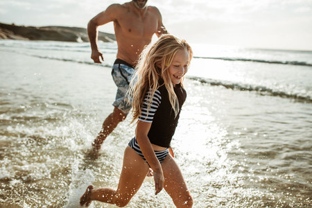 Girl running in water with her father at the beach
