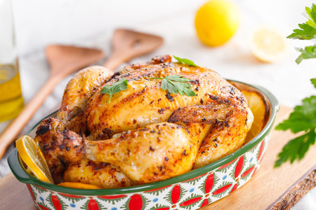 Whole roasted chicken with fresh parsley and lemon wedges in a festive dish