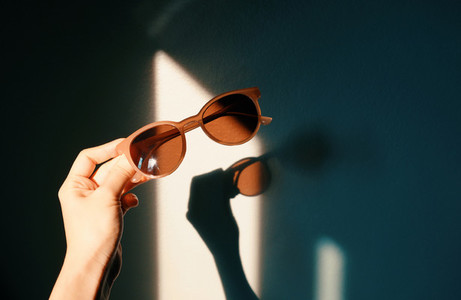 Woman hand holding fashionable sunglasses with shade of sunlight