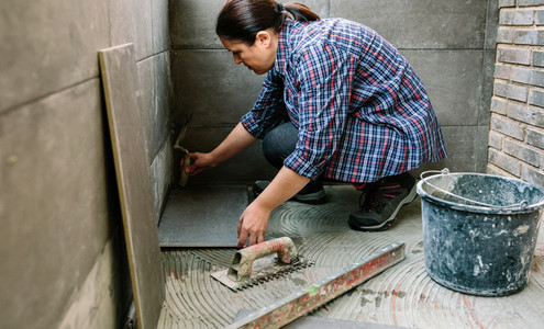 Female manual worker laying a new tile floor