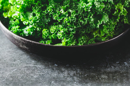 Fresh curly kale salad in a black plate over dark rustic background