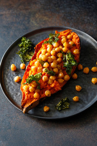 Baked sweet potato stuffed with chickpea and crunchy kale on a black plate  Vegan tasty dish for dinner or lunch